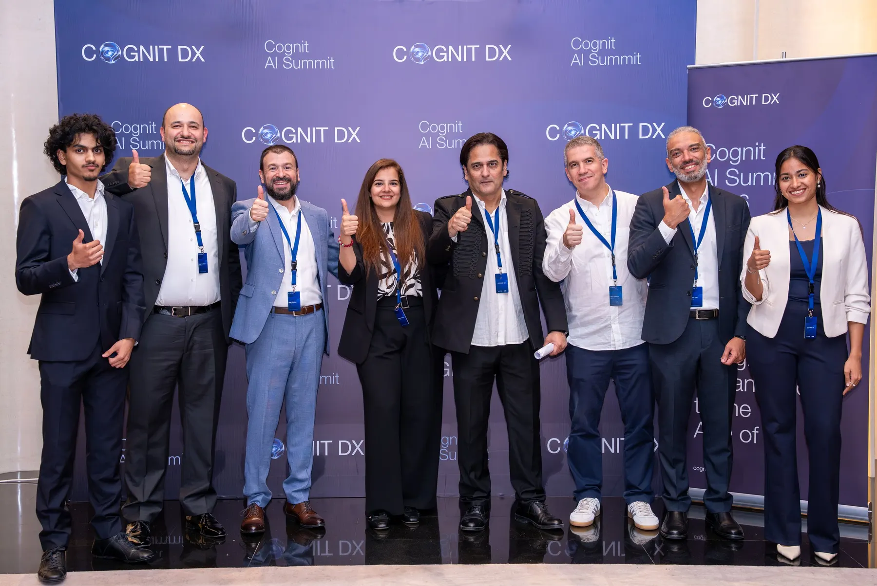 The Cognit team at the Cognit AI Summit 2026 photo wall, thumbs up to the camera