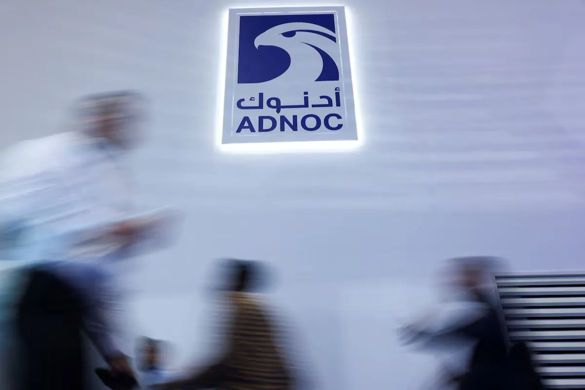 The ADNOC logo lit on a wall as people pass, blurred by motion